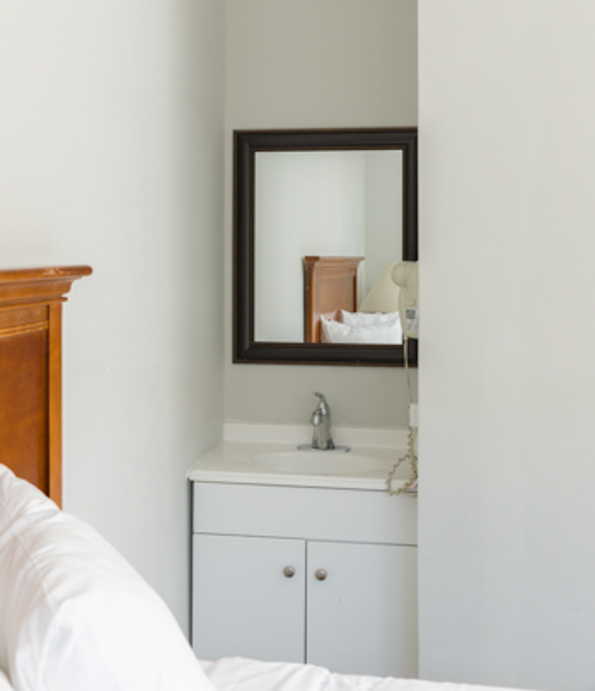 a small hotel room with a bed, sink, and mirror