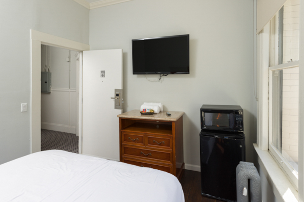 A hotel room with a bed, TV, mini fridge, and window