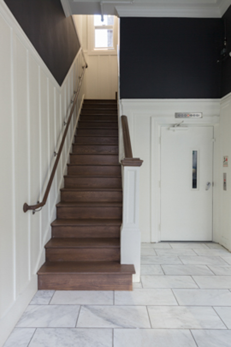 A staircase with a wooden handrail and white walls leading to a door