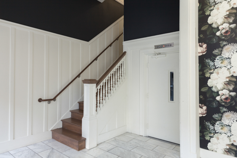 A lobby with a staircase, elevator, and floral wallpaper