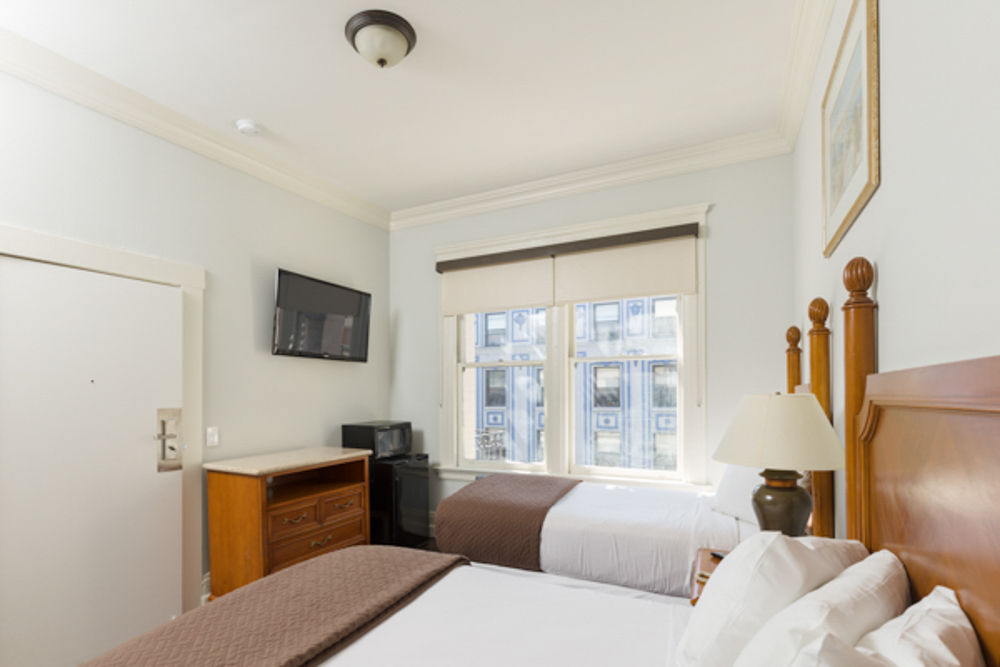 A hotel room with two beds, a window, a TV, and a dresser